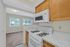 Bright kitchen with modern appliances, adjacent to a carpeted living area with large windows offering lush green views.