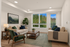Elegant living room with large windows offering a serene view of lush greenery, featuring comfortable sofas, modern decor, and natural light.