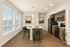 Sleek modern kitchen with stainless steel appliances, elegant wood cabinetry, and a chic island with green barstools, bathed in natural light from large windows.