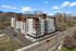Modern apartment building with multiple balconies, set against a lush natural backdrop, featuring spacious parking and convenient street access.