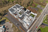 Aerial view of a modern apartment complex with solar panels, rooftop garden, and ample parking, surrounded by lush greenery.