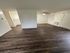 Modern apartment interior featuring stylish dark wood flooring, a ceiling fan, and ample natural light.