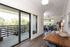 Elegant apartment showcasing a spacious living room with large windows, modern wooden dining table, and access to a sunlit balcony with lush views.
