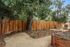 Charming backyard oasis with lush greenery, stylish wooden fencing, and inviting lounge chairs under a sprawling tree.