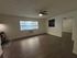 Bright and airy living space with elegant wood flooring, large window, and modern ceiling fan, leading to an inviting kitchen and adjacent room.
