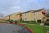 Charming apartment complex with beige siding, surrounded by lush greenery and neatly trimmed hedges, offering serene suburban living.