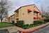 Charming beige apartment complex with vibrant red accents, featuring lush greenery and modern architectural design.