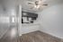 Modern apartment interior showcasing a sleek kitchen with grey cabinetry, open bar seating, and bright living area with wood-style flooring and ceiling fan.