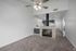 Modern living room with tiled fireplace, and ceiling fan, leading to a sleek kitchen and hallway.
