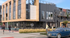 Charming urban apartment building with modern design, featuring outdoor seating at a cozy caf&eacute; and vibrant street life.