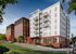 Modern apartment complex with a blend of brick and white paneling, featuring multiple balconies, lush landscaping, and a scenic neighborhood street.