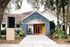 Inviting leasing office entrance with vibrant pomelo-colored doors, surrounded by lush greenery and palm trees.