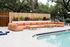 Inviting outdoor pool area with stylish orange lounge seating and lush green backdrop.