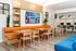Vibrant community room with modern decor, featuring orange seating, wooden tables, and a relaxing workspace with computers.