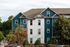 Elegant multi-story residential building with blue and white siding, surrounded by lush greenery and well-maintained shrubs.