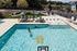 Inviting outdoor swimming pool area with comfortable lounge chairs and shaded picnic tables, surrounded by lush greenery and vibrant community amenities.