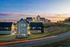 Scenic view of modern hillside homes illuminated at sunset, set against a picturesque sky, highlighting tranquil and contemporary neighborhood living.