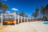 Inviting outdoor lounge area with vibrant orange seating, elegant cabanas, and a sparkling pool set against a backdrop of lush trees under a bright blue sky.