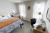 Bright and modern bedroom with cozy bedding, stylish desk setup, and abundant natural light from tall windows.