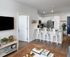 Bright and modern open-concept living space featuring a stylish kitchen with white cabinets and stainless steel appliances, complemented by elegant pendant lighting and bar seating.