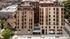 Modern urban apartment building with stylish brick facade, large windows, and rooftop terraces in a vibrant city setting.