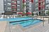 Modern apartment complex featuring a luxurious outdoor pool area with stylish loungers, vibrant red umbrellas, and lush palm trees.
