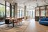 Modern communal space featuring large windows, a stylish wood table with leather chairs, and a cozy lounge area with contemporary furniture.