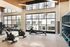 Modern gym with large windows, featuring bright interior, stationary bikes, rowing machine, and weights on sleek shelves.