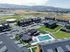 Aerial view of modern apartment complex with lush green spaces, a sparkling swimming pool, and scenic mountain backdrop.