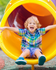Joyful child sliding down a vibrant yellow playground slide, exuding happiness and energy on a sunny day.