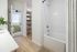 Modern bathroom featuring a pristine white bathtub, a stylish striped shower curtain, and a view into a cozy bedroom with soft green accents.