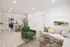 Bright and modern open-concept living space featuring a sleek kitchen with light wood cabinets and stainless steel appliances, cozy living area with comfortable green and beige furnishings, and stylish decor.