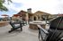 Inviting outdoor patio with Adirondack chairs surrounding a central fire pit, complemented by stylish red umbrellas and a warm, stone-accented clubhouse.