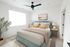 Bright and airy bedroom with a plush, light blue bed, stylish decor, and abundant natural light from a large window.