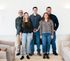 A welcoming group of five individuals standing in a chic, modern living room with stylish seating and soft lighting.