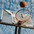 Dynamic basketball action with a ball soaring towards the hoop against a vibrant blue sky backdrop.