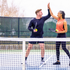 Energetic couple celebrating with a high-five on a pickleball court, holding paddles and a ball, showcasing a vibrant and active lifestyle.