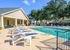 Luxurious outdoor pool area with elegant lounge chairs and shaded seating, surrounded by lush greenery and a stylish clubhouse, perfect for relaxation.