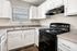 Modern kitchen with sleek black appliances, ample white cabinetry, and elegant countertops, filled with natural light.