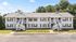 Charming two-story apartment building with white siding, featuring elegant staircases and lush green surroundings.