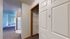 Bright apartment hallway showcasing a spacious closet with wire shelving, leading to an open kitchen with modern appliances and a cozy living area filled with natural light.