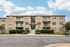 Charming brick apartment building with spacious balconies, surrounded by lush greenery under a bright blue sky.