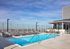 Daytime view of AMLI West Loop rooftop swimming pool with lounge chairs, a glass rail, and a dining area, all overlooking the city skyline.