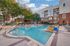 Resort-style swimming pool with white in-water loungers, umbrellas, cushioned seating and brick buildings at AMLI Frisco Crossing apartments.