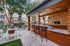 Covered outdoor lounge with bar seating, pendant lights and flat screen TV at AMLI Frisco Crossing apartments, with tables and trees nearby.