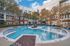 Courtyard view of round resort-style pool with blue lounge chairs, trees, and red brick buildings at AMLI Frisco Crossing apartments.