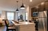 Modern kitchen and living area with a sleek island, elegant lighting, and stainless steel appliances creating a warm, inviting space.