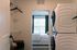 Chic apartment laundry area featuring a modern stacked washer and dryer, leading to a cozy sunlit bedroom with large windows.