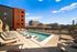 Modern urban apartment complex featuring a luxurious rooftop pool with city views, surrounded by stylish lounge chairs, under a vibrant blue sky.