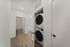 Chic apartment hallway featuring a modern stacked washer and dryer, elegant wood flooring, and access to a stylish bathroom with subway tile accent.